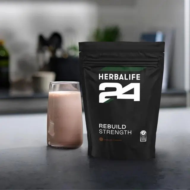 Herbalife 24 rebuild strength supplement package with a glass of powder on a kitchen counter.
