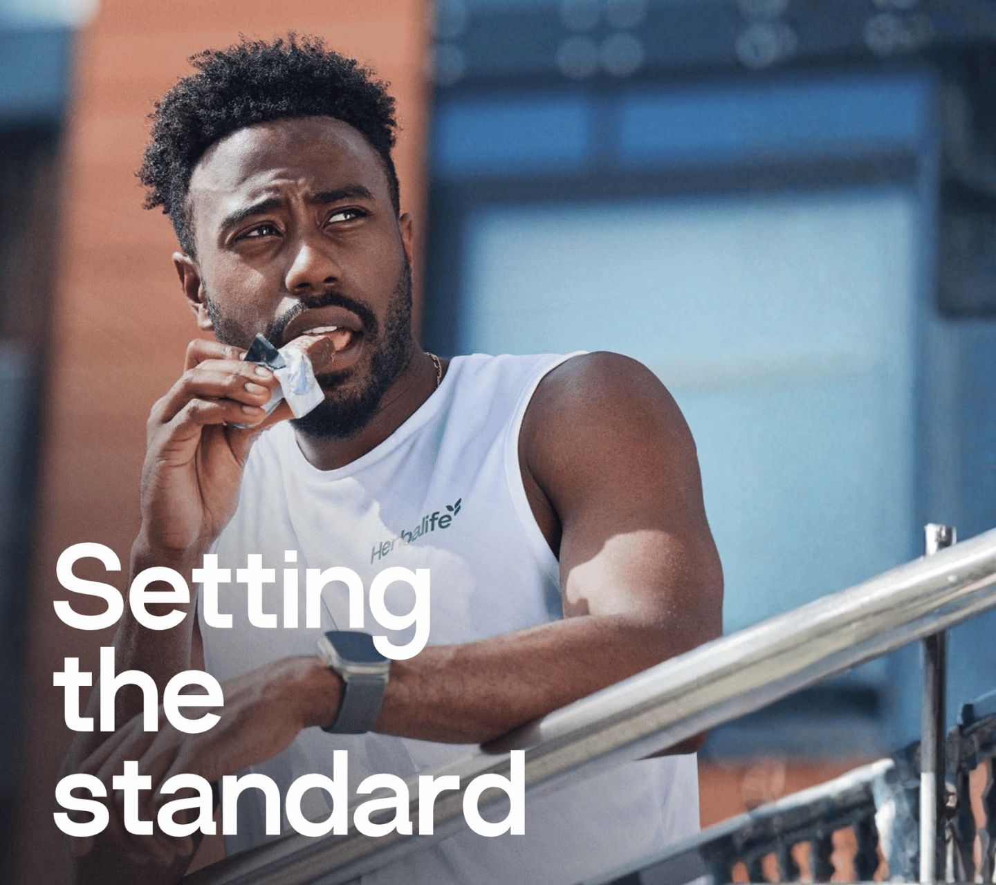 Man in a white tank top holding a white object with text 'Setting the standard' on a blurred background
